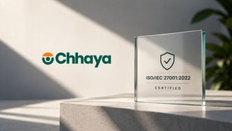 Chhaya logo on a sunlit wall next to a glass plaque with a shield and checkmark that reads “ISO/IEC 27001:2022 Certified,” resting on a stone ledge