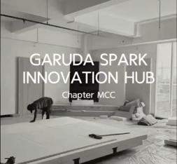 "Black-and-white photo of a SECHA construction site: two workers installing flooring in an unfinished open-plan interior with exposed ceiling ducts and large windows. Overlaid text reads 'Garuda Spark Innovation Hub — Chapter MCC.'"